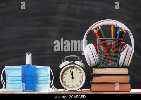Education concept. Back to school. Schoolboy set. Stack of books pencils glasses alarm clock headphones protective medical masks sanitizer on a black Stock Photo