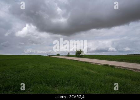 A road crosses the green fields under a stormy sky, Uclés, Cuenca, Spain Stock Photo