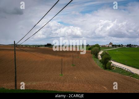 Wired poles cross the fields under a cloudy sky and parallel to the road, Uclés, Cuenca, Spain Stock Photo
