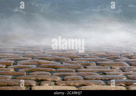 long exposure photo of waves breaking over cobbled slipway Stock Photo