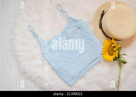 Blue lace top, straw hat and sunflower. On white fur, top view Stock Photo