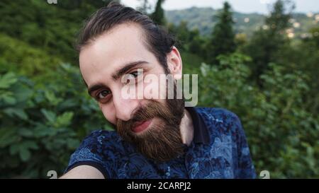 Young and long bun hair and long beard hipster man with making video call with camera in hands POV close-up Stock Photo