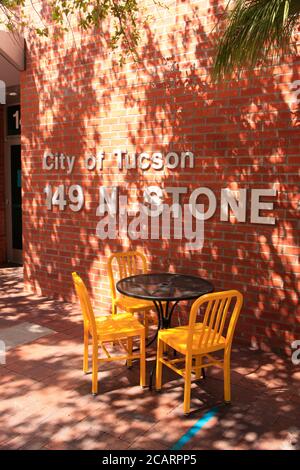 Black table and four yellow chairs outside in the mottled sunlight at 149 N Stone in downtown Tucson AZ Stock Photo
