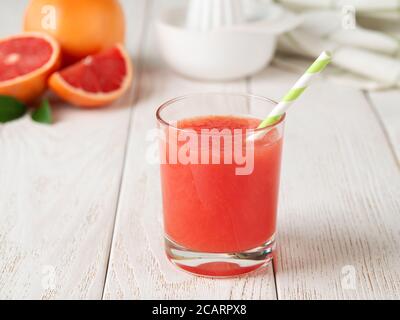 Glass of freshly squeezed grapefruit juice with pulp and drinking straw on a white wooden table. Vegetarian, raw food diet and healthy eating. Stock Photo