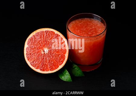 Half of fresh ripe grapefruit and glass of freshly squeezed grapefruit juice with pulp on black background. Low key image. Vegetarian, raw food diet. Stock Photo
