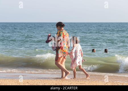 Punta Umbria, Huelva, Spain - August 7, 2020: Mother and daughter are walking by the beach wearing protective or medical face masks. New normal in Spa Stock Photo