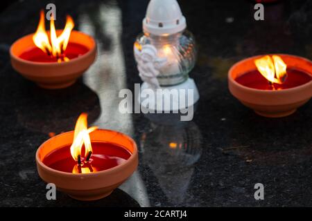 Three traditional burning grave candles and decorative one on a grave during All Souls' Day Stock Photo