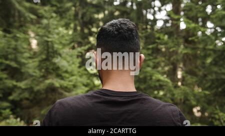 Young man wearing a black t-shirt, walking through the forest, back view Stock Photo