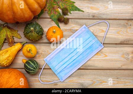Thanksgiving 2020, coronavirus days, Protective face mask and colorful pumpkins on wooden background. COVID 19 spread prevention measure Stock Photo