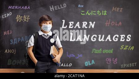 Schoolboy with a protective mask in front of a blackboard with text learn languages Stock Photo