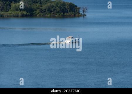 A small recreational powerboat heading out across a calm lake with a wooded peninsula in the background. Stock Photo