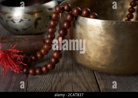 Tibetan singing copper bowl with a wooden clapper and prayer rosary on a gray wooden table, close up