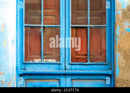 Blue weathered window frame with broken glass and aged wall sections, old derelct and abandoned house detail in Latino district Stock Photo