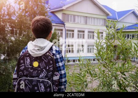 Irkutsk, Russia - August 05, 2020: Child boy with bag looks to elementary school. Back view Stock Photo
