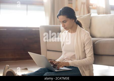 Focused young freelancer sitting on floor working remotely on computer. Stock Photo