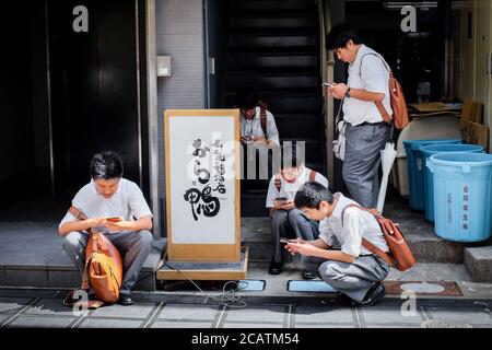 Students in Japan engrossed in their smartphones. Stock Photo