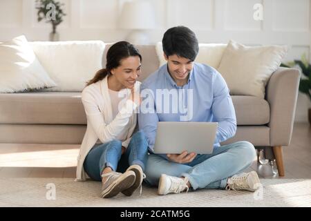 Smiling young family couple using computer together indoors. Stock Photo