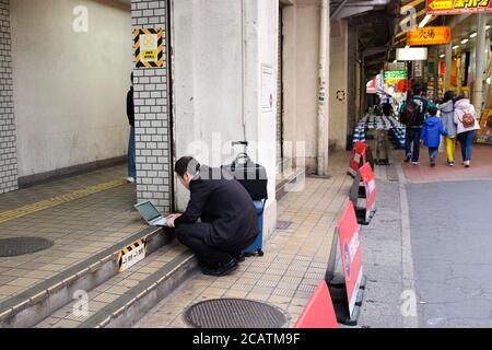 A salaryman in Japan works on his laptop while out in the street. Stock Photo