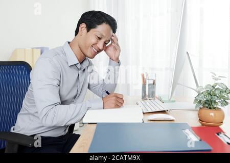 Smiling young businessman writing down his ideas and plans for the day Stock Photo