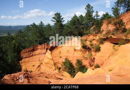 View of colorful orange ochre cliffs with pine trees and blue sky at the natural regional park in Roussillon, Vaucluse, Luberon, France Stock Photo