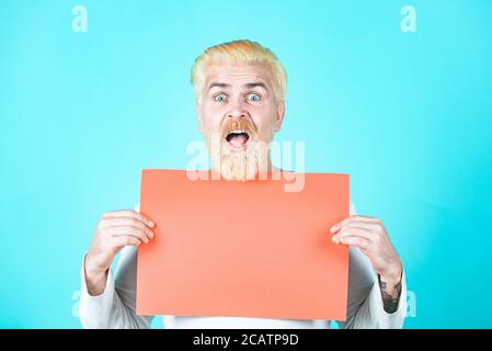 Surprised bearded man holding empty paper. Discount sale or season sales. Business man holding a blank banner and looking down to copy space. Stock Photo