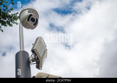 CCTV dome security camera and LED floodlight on a pole in sky Stock Photo