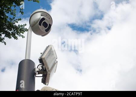 CCTV dome security camera and LED floodlight on a pole in sky Stock Photo