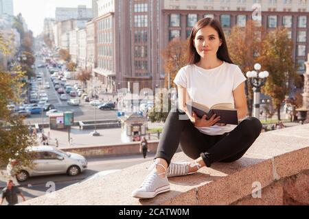 Full length shot of a happy beautiful female student enjoying reading a book in the city center, copy space Stock Photo