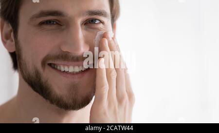 Close up smiling young man applying moisturizing face cream Stock Photo