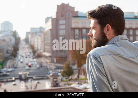 Cropped rear view shot of a bearded young man looking away thoughtfully, city streets on the background Stock Photo