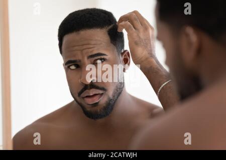 Close up anxious unhappy African American man checking hair Stock Photo