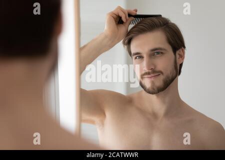 Close up mirror reflection handsome young man combing hair Stock Photo
