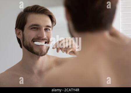 Close up mirror reflection satisfied young man brushing teeth Stock Photo