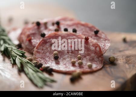 Sliced salame milano sausage on olive wood board with rosemary and pepper Stock Photo