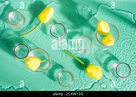 Decorative composition with glass vases with flowers on a turquoise color background with water under glass texture, copy space and shadows. Stock Photo