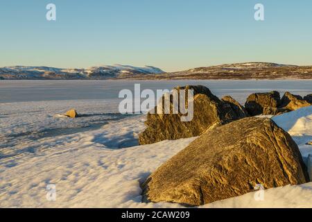 Snowy landscape in spring time with mountains in background, frozen lake Torneträsk, big rocks in foreground,  Kiruna county, Swedish Lapland, Sweden Stock Photo