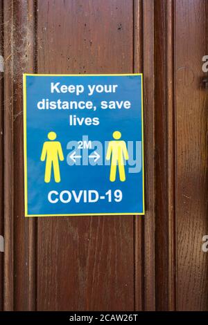 Blue and yellow 2m social distancing reminder sign on a door in High Street, Chipping Campden in the Cotswolds, Glos: keep your distance, save lives Stock Photo