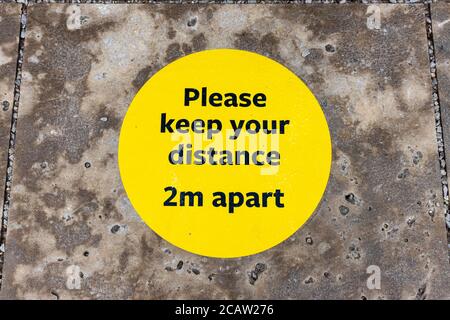 Yellow and black 2m social distancing floor sticker reminder sign at RHS Garden, Wisley, Surrey Stock Photo