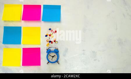 Several blank colorful notes with copy space for text on light background. Blue alarm clock, push pins. Stock Photo