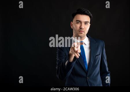 Portrait of business man wearing blue business suit and tie doing I am watching you gesture posing on isolated black background with copy space advert Stock Photo