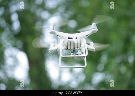 Quadcopter with camera aboard flying in front of the blurred leaves background Stock Photo