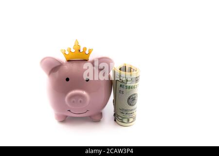 Pink piggy bank with golden crown and stack of US dollars on the right, isolated over white background with copy space, cash is king concept image