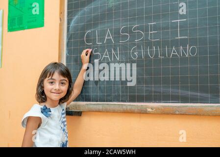 Young girl on her first day of elementary school in the classroom writing on the chalkboard. Stock Photo