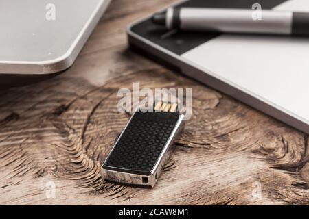 Close-up, flash drive, laptop and graphics tablet lie on a wooden office table. Work in office. Stock Photo