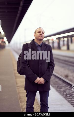 Train Station. Mature man in business clothes and coat is standing on platform Stock Photo