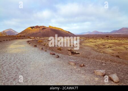 Barren volcanic landscape with a lonely path at El Cuervo ("The Raven") volcano in the Los Volcanes natural park in Lanzarote, Canary Islands, Spain. Stock Photo