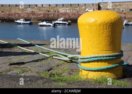 Ropes Aroung Yellow Mooring Bollard and Small Fishing Boats in the Water at Victoria Harbour in Dunbar Stock Photo