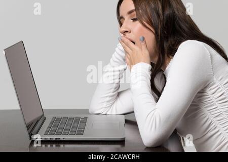 Fatigue, tedium, boredom at work and sleep deprivation concept. Studio portrait of sleepy exhausted tired young woman yawning, sitting at the table an Stock Photo