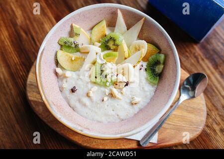 Oatmeal with fruits and nuts served in a bowl on a board with a teaspoon Stock Photo