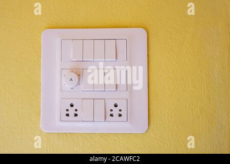 a modern electrical light switch, dimmer & outlet panel isolated on yellow wall Stock Photo